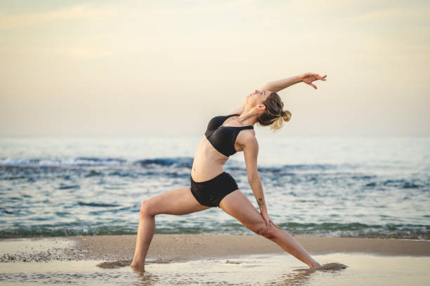 Young Woman Practicing Reverse Warrior Yoga Pose On The Beach stock photo