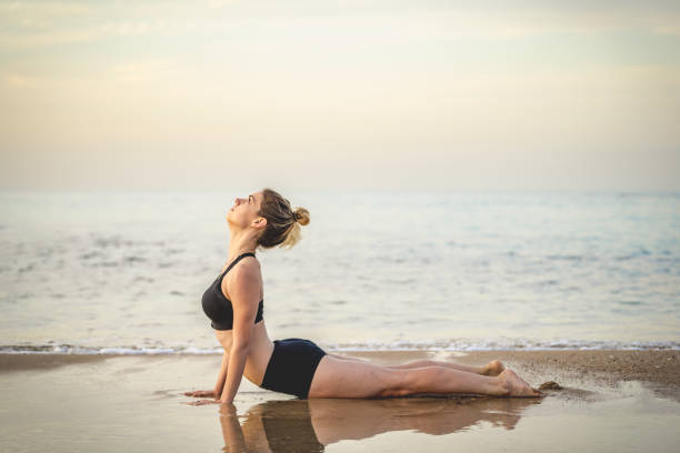 Young Woman Practicing Upward Facing Dog Yoga Pose On The Beach stock photo