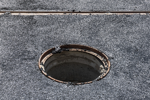 A deep manhole without a cover on the road while laying a new asphalt presents a danger to pedestrians and cars