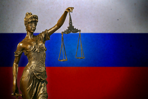 Close-up of a small bronze statuette of Lady Justice before a Russian flag.