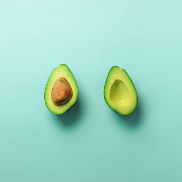 istock Green avocado halves with seed on blue pastel background. Creative minimal flat lay style with copy space. Summer food concept. Top view. Pop art design. Square crop 1003071212