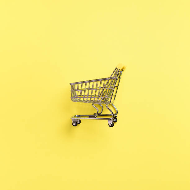 istock Shopping cart on yellow background. Minimalism style. Creative design. Top view with copy space. Shop trolley at supermarket. Sale, discount, shopaholism concept. Consumer society trend 1003087044