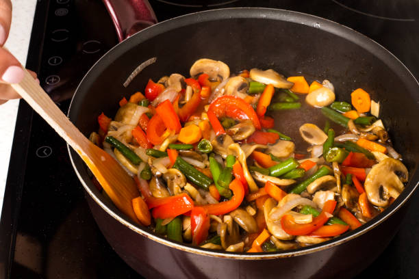 Stirring vegetables with mushrooms in a frying pan on a dark background. Cooking food