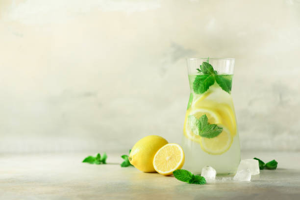 istock Detox water with mint, lemon on grey background. Banner with copy space, sunlight bokeh. Citrus lemonade. Summer fruit infused water. Refreshing homemade cocktail, selective focus 1003107580
