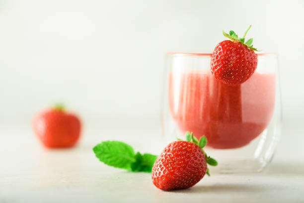 Red strawberry milkshake in glass on grey background with copy space. Summer food concept, vegan diet. Pink smoothie with fresh berries
