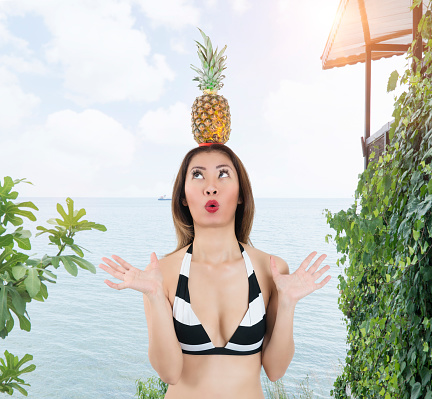 Asian woman with bikini carrying pineapple on head