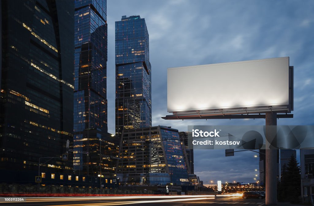 Blank billboard at twilight next to skyscrapers. 3d rendering Blank billboard at night time in the city next to skyscrapers and road with lights on the frame. 3d rendering Billboard Stock Photo