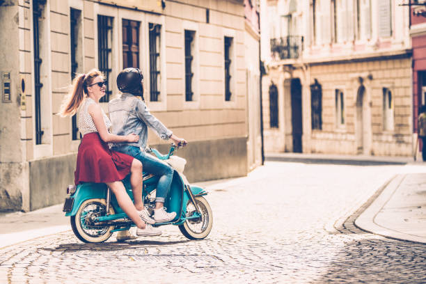 Young Lesbian Couple Driving Old-fashioned Motor Scooter on Italian City Streets Young Lesbian Couple Driving Old-fashioned Motor Scooter on Italian City Streets. moped stock pictures, royalty-free photos & images