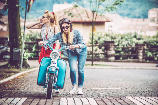 istock Young Women Pushing Broken Down Motor Scooter and Calling for Help 1003129632