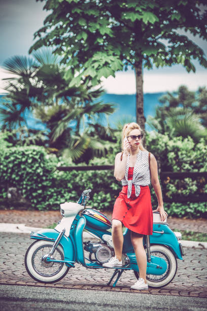 istock Young Woman Leaning on Old-fashioned Motor Scooter and Using Mobile Phone 1003129638