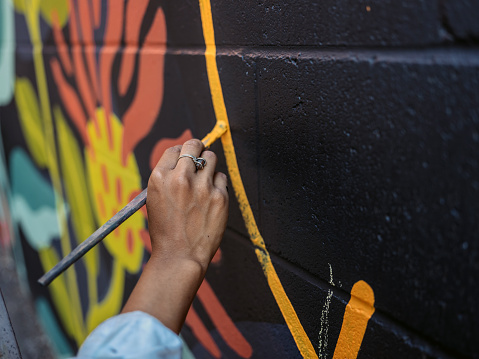 Hand close up of Young Asian woman, mural artist creating wall art at the urban setting.