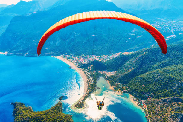 paragliding in the sky. paraglider tandem flying over the sea with blue water and mountains in bright sunny day. aerial view of paraglider and blue lagoon in oludeniz, turkey. extreme sport. landscape - airplane sky extreme sports men imagens e fotografias de stock