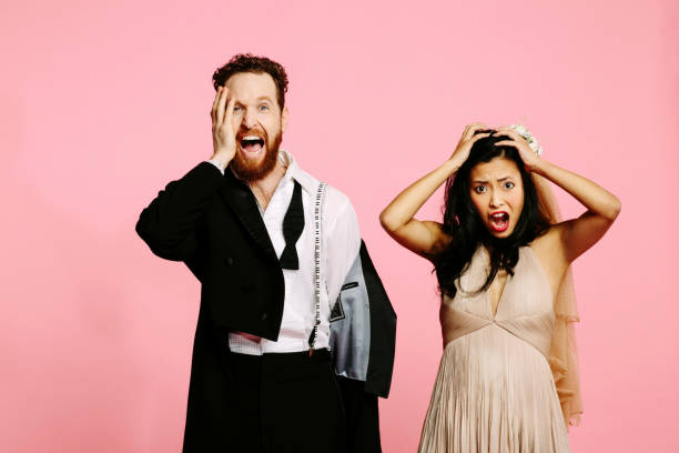 A wedding nightmare- A screaming and shocked bride and groom holding their heads, isolated on pink studio background