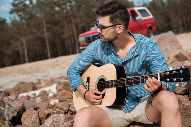 istock young man playing acoustic guitar outdoors, red jeep on background 1003166328