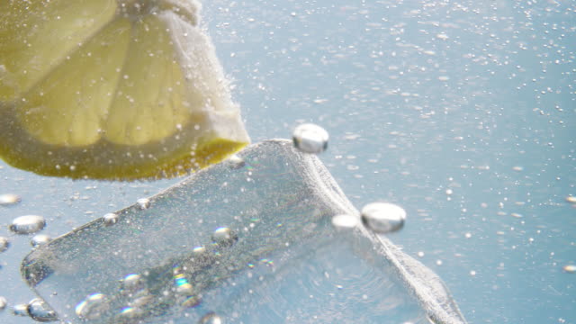 Lemon slice falling down in water with ice cube inside