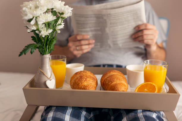 istock Man having breakfast in bed and reading newspapers 1003172660