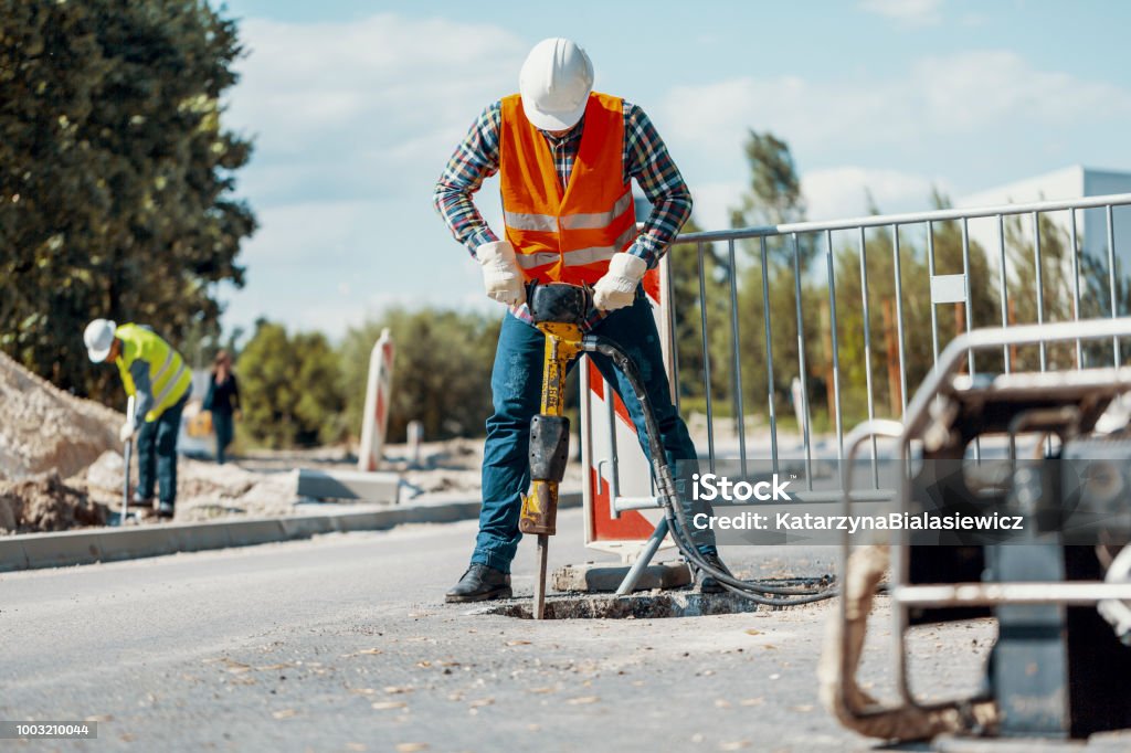 Worker in reflective vest with drill repairing street during roadworks Road Stock Photo