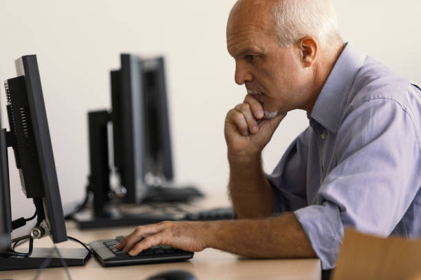 Profile view of senior man working at computer. Profile view of Business man working away at desktop computer. computer shop stock pictures, royalty-free photos & images