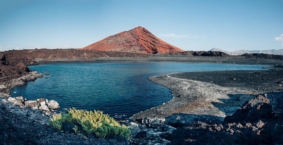 Panoramic view of unique volcanic landscape in Lanzarote island. Black sand, lake and and red mountain. Playa Bermeja. Travel destination. Nature background. unesco heritage. Canary Islands