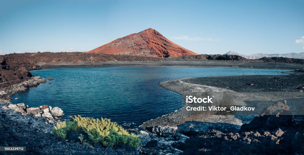 Panoramic view of unique volcanic nature of Lanzarote island Panoramic view of unique volcanic landscape in Lanzarote island. Black sand, lake and and red mountain. Playa Bermeja. Travel destination. Nature background. unesco heritage. Canary Islands Lanzarote Stock Photo