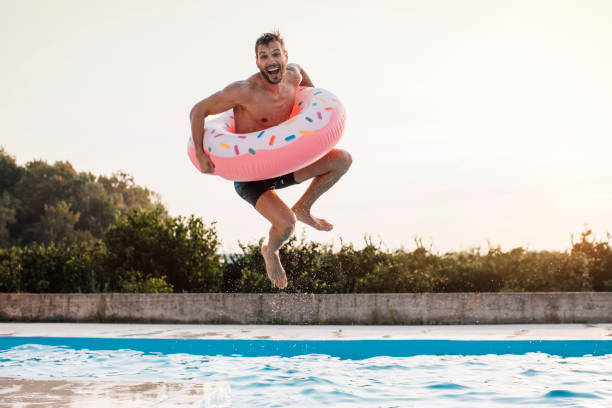A jump with inflatable ring Young man enjoying time at the swimming pool jumping into the water with inflatable ring swimming pool stock pictures, royalty-free photos & images