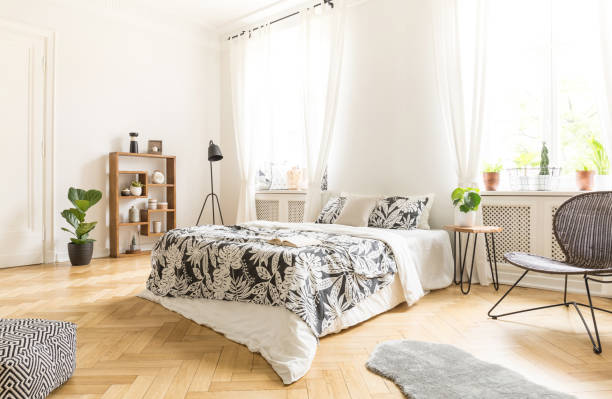 istock Black chair near bed with patterned sheets in white bedroom interior with pouf and fur. Real photo 1003246190