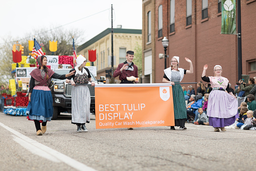 Holland, Michigan, USA - May 12, 2018 A man and women wearing traditional dutch clothing carrying a banner that says Best tulip display at the Muziek Parade, during the Tulip Time Festival