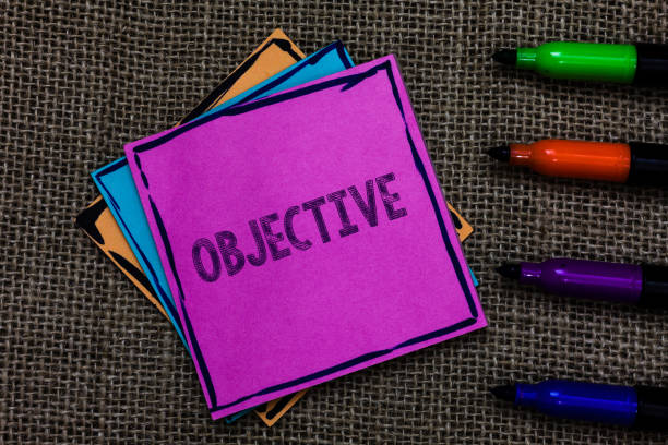 istock Text sign showing Objective. Conceptual photo Goal planned to be achieved Desired target Company mission Multiple colour sticky remember cards pen script marker jute background. 1003278446
