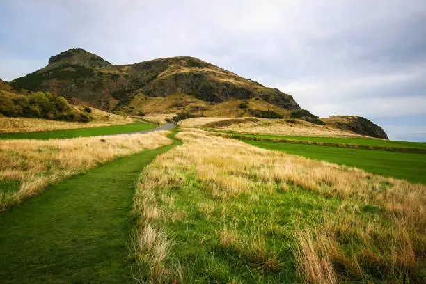 Photo of Holyrood Park, green and yellow grass with Arthur's Seat in the background on overcast autumn day. Edinburgh, Scotland