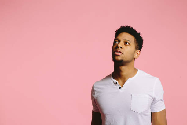 istock Young man looking up with curiosity and slightly open mouth, on pink 1003312474