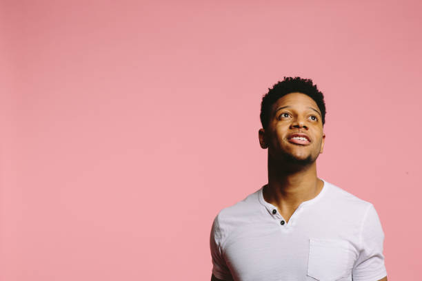istock Young man smiling and looking up out of frame, on pink 1003312484