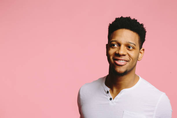 istock Young man in white smiling and looking sideways  out of frame, on pink 1003312506