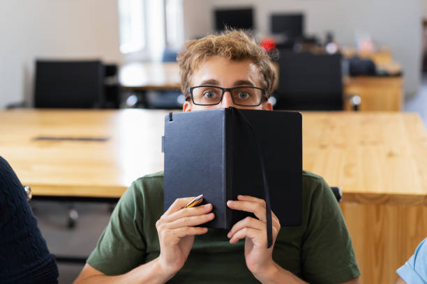 estudiante hombre asustado escondiéndose detrás de notebook - men hiding fear terrified fotografías e imágenes de stock