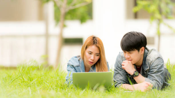 education, school and people concept - Cheerful university students with laptop on group of students in background at each other at school; Asia university. stock photo