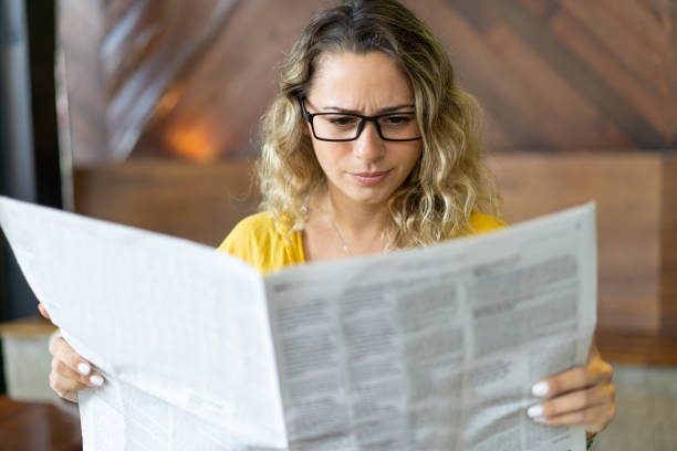新聞の求人広告を読む若い女性の顔をしかめ - young adult reading newspaper the media ストックフォトと画像
