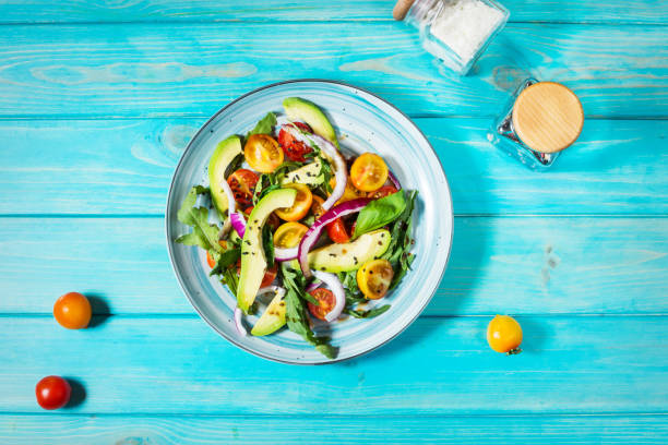 istock Salad with tomatoes and avocado on blue wooden background. 1003335662