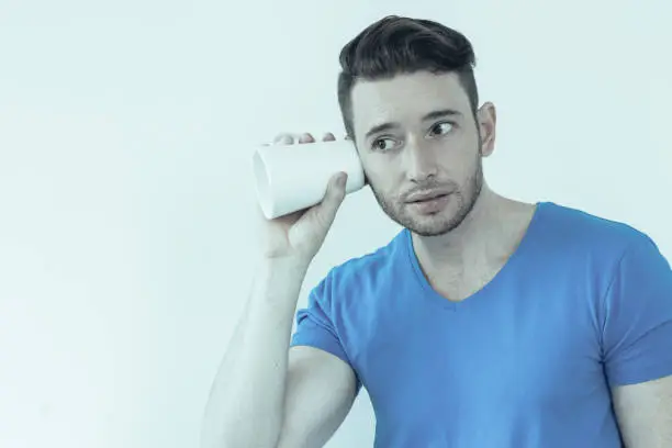 Photo of Concentrated young man eavesdropping with mug