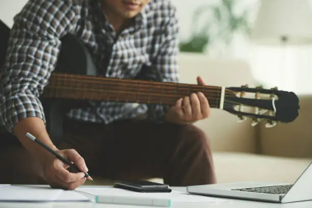 Cropped image of composer playing guitar and taking notes
