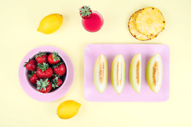 Fresh strawberries in bowl and melon on pastel yellow background. Top view point.
