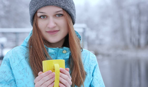 jeune fille se réchauffe ses mains sur une tasse de thé ou café se tenant debout sur le fond d’une forêt en hiver sur la rive du fleuve - beach on child the photos et images de collection