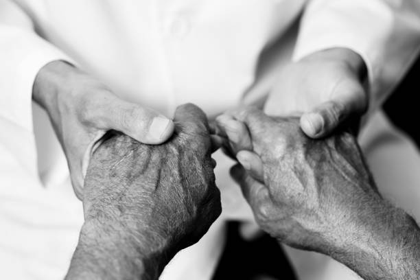 man holding the hands of a senior man closeup of a caucasian man, in a white coat, holding the hands of a senior caucasian man, in black and white physical therapist photos stock pictures, royalty-free photos & images