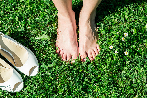 Barefoot bride standing on green grass in park with new leather shoes near