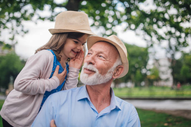 ragazza sorridente che sussurra a suo nonno - whispering grandparent child grandfather foto e immagini stock