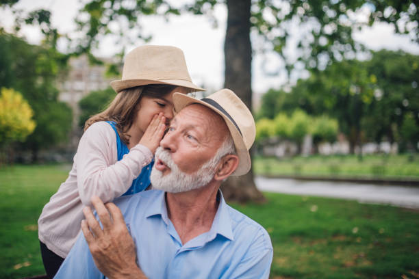 chica joven susurrando secretos a su abuelo - whispering grandparent child grandfather fotografías e imágenes de stock