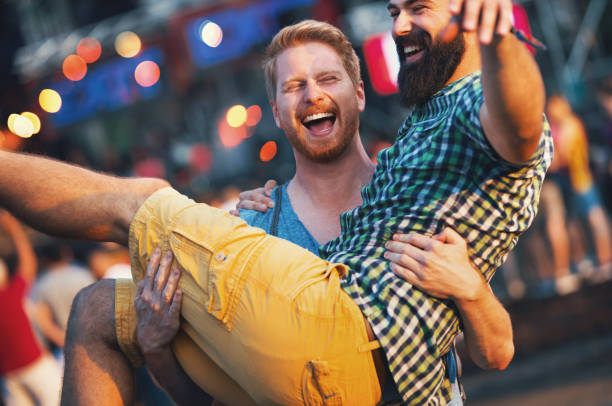 Friends having fun at a concert. Closeup of couple of young adults having fun at an open air concert on a sunny afternoon. The guy is carrying and spinning his friend. Blurry people in background. common couple men outdoors stock pictures, royalty-free photos & images