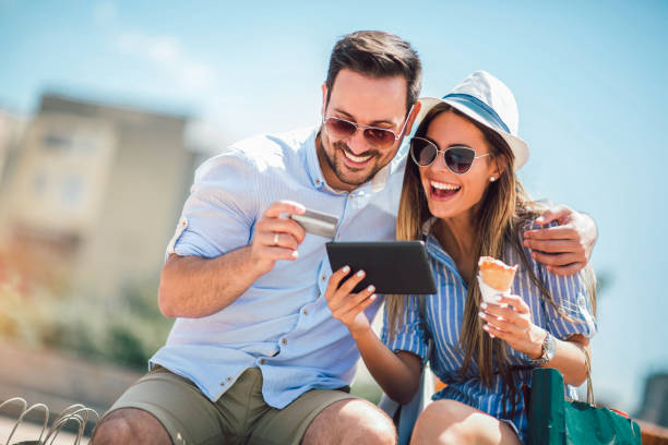 happy couple paying on line with credit card and digital tablet on the street - love couple city life urban scene imagens e fotografias de stock