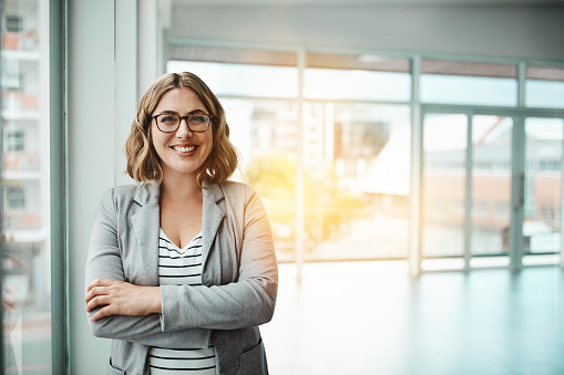 Portrait of mid adult business woman in the modern office. Successful businesswoman standing in the office, with arms crossed looking at camera and smiling