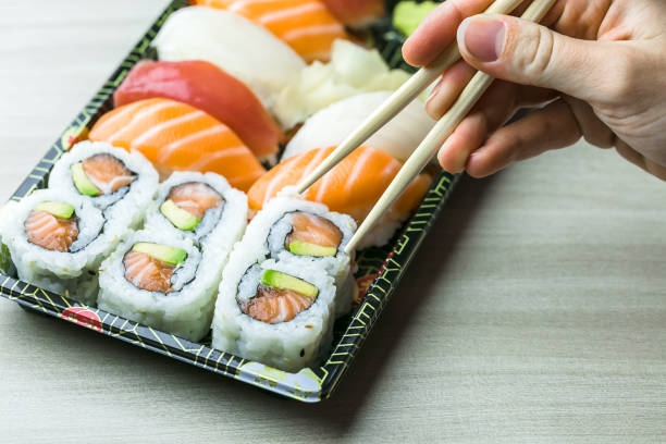 istock Cropped Hand Having Sushi And Sashimi In Box On Table 1003399210