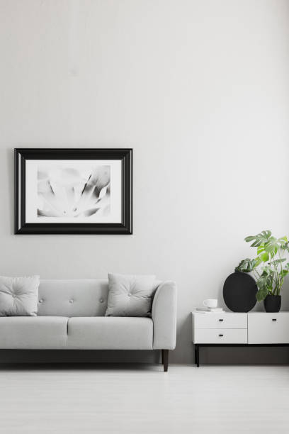 istock Photo in a black, thick frame on a gray wall, white sideboard and a gray sofa in a stylish living room interior with place for a Photo in a black, thick frame on a gray wall, white sideboard and a comfy sofa in a stylish living room interior with place fo 1003399458