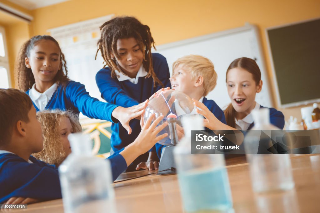 School kids touching plasma ball during physics lesson at school Group of student listening to female teacher showing plasma ball during physics lesson. Plasma Ball Stock Photo